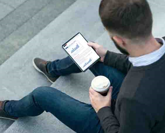 man holding a coffee and reading news alert on an tablet