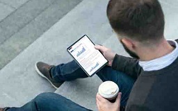 Man sat on steps looking at his tablet with a coffee in the other hand